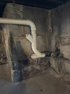 Wet basement fieldstone foundation wall with visible moisture stains and drainage pipe
