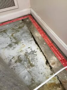 Wide basement floor crack caused by foundation settlement with visible moisture damage along the concrete slab.