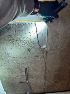 Vertical crack in a concrete basement foundation wall being inspected with a flashlight