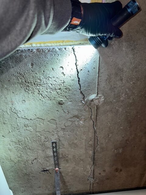 Vertical crack in a concrete basement foundation wall being inspected with a flashlight