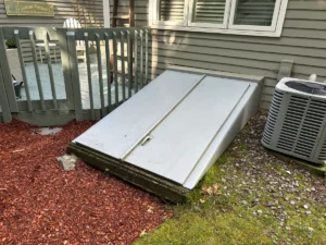 Original light-gray bulkhead doors on a concrete basement entrance beside a porch in Nashua, NH.